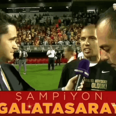 Man Talking Into Microphone In Front Of Galatasaray Sign GIF