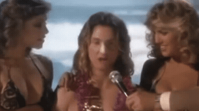 Man Talking Into Microphone With Two Women In Bikinis GIF