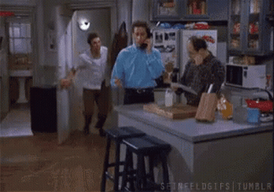 Man Talking On Phone While Another Man Dances In Kitchen GIF