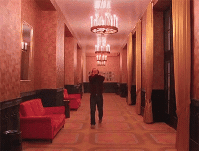 Man Walking Down Hallway With Chandelier And Red Couch GIF