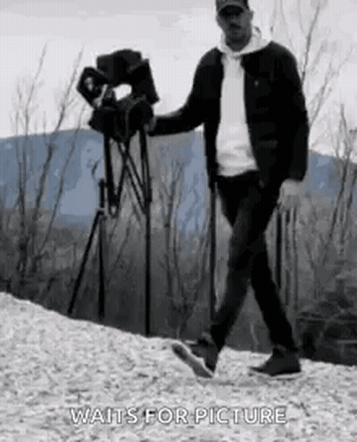 Man Walking Down Hill Holding Camera And Tripod GIF