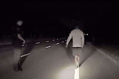 Man Walking Down Road At Night With Police Officer Behind GIF