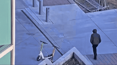 Man Walking Down Sidewalk With Parked Scooters GIF