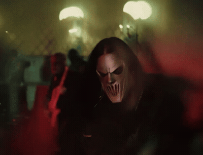Man Wearing Mask Standing In Dark Room With People Behind GIF