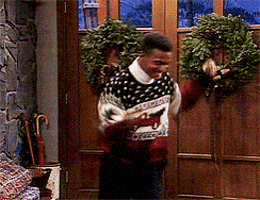 Man Wearing Sweater With Horse Stands In Front Of Door With Wreath GIF