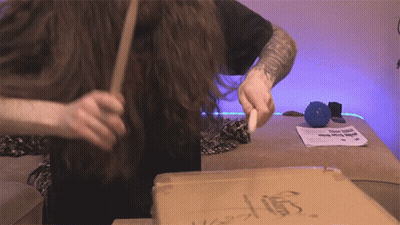 Man With Arm Tattoo Holding Stick In Front Of Cardboard Box Saying Stump GIF