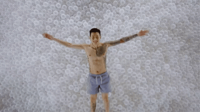 Man With Arm Tattoo Lying In Plastic Balls GIF