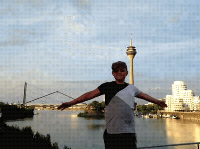 Man With Arms Outstretched In Front Of River And Tower GIF