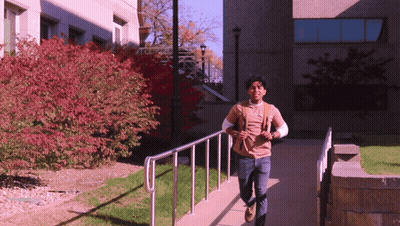 Man With Backpack Walking Down Sidewalk GIF