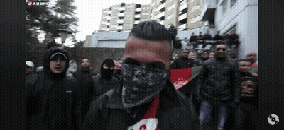 Man With Bandana Stands In Front Of Group GIF
