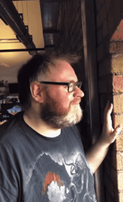 Man With Beard And Glasses Leaning Against Wall GIF