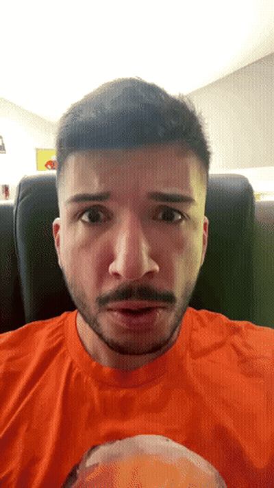 Man With Beard In Orange Shirt Looking At Camera GIF