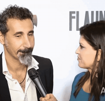 Man With Beard Interviewed By Woman In Front Of Flaunt Wall GIF