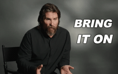 Man With Beard Sitting In Front Of Bring It On Sign GIF