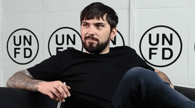 Man With Beard Sitting On Couch In Front Of Un Fd Wall GIF