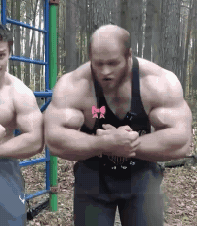 Man With Bow On Chest Flexing Muscles Next To Another Man GIF