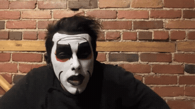 Man With Clown Face Sitting By Brick Wall GIF