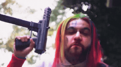 Man With Colorful Hair And Beard Holding Gun GIF