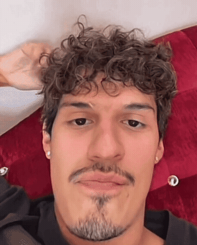 Man With Curly Hair And Beard Laying On Bed Making Funny Face GIF