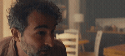 Man With Curly Hair And Beard Sitting At Table GIF