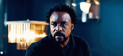 Man With Curly Hair And Beard Sitting In Dark Room GIF