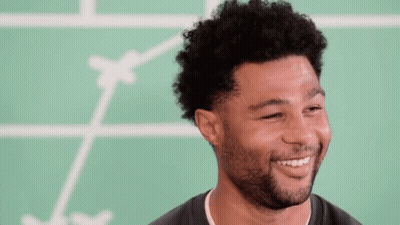 Man With Curly Hair And Beard Smiling In Front Of Green Board GIF