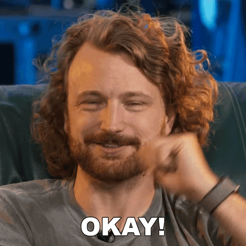 Man With Curly Hair And Beard Smiling Says Okay GIF
