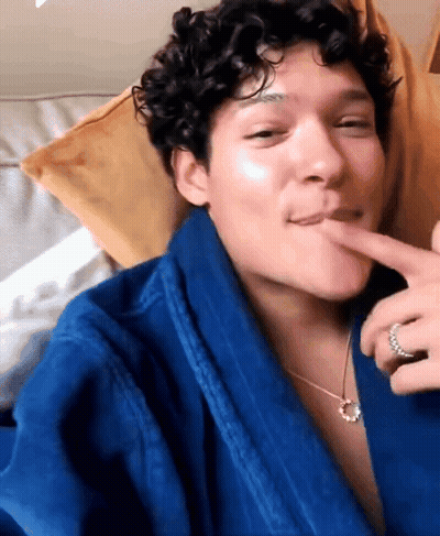 Man With Curly Hair In Blue Robe And Necklace Licking Lips GIF