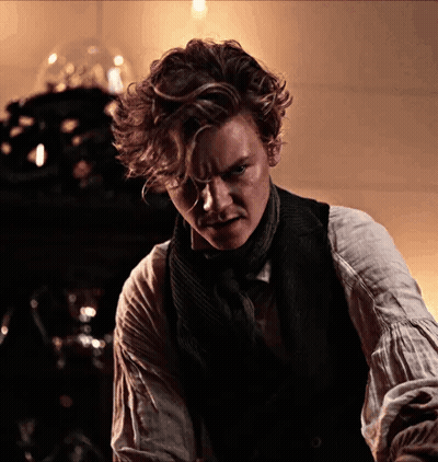 Man With Curly Hair In Vest And Scarf Looking At Camera GIF