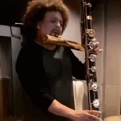 Man With Curly Hair Playing Bassoon In Dark Room GIF