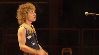 Man With Curly Hair Singing In Blue And Gold Outfit GIF