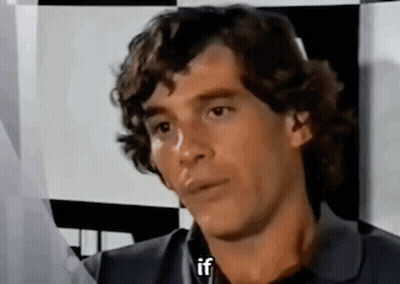 Man With Curly Hair Sitting In Front Of Checkered Wall Talking GIF