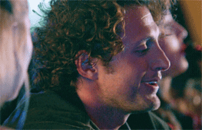 Man With Curly Hair Smiling In Dark Room GIF