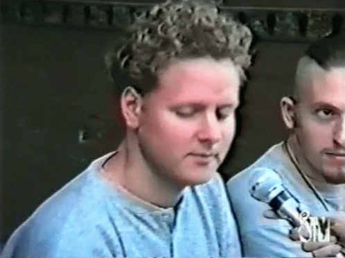 Man With Curly Hair Talking Into Microphone Another Man Looks On GIF