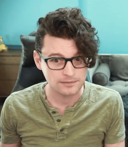 Man With Curly Hair Wearing Glasses And Green Shirt Looks At Camera GIF
