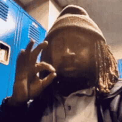 Man With Dreadlocks And Beanie Making Peace Sign At Blue Lockers GIF