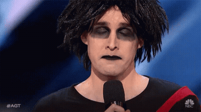 Man With Dreadlocks And Black Makeup Holding Microphone In Wig GIF