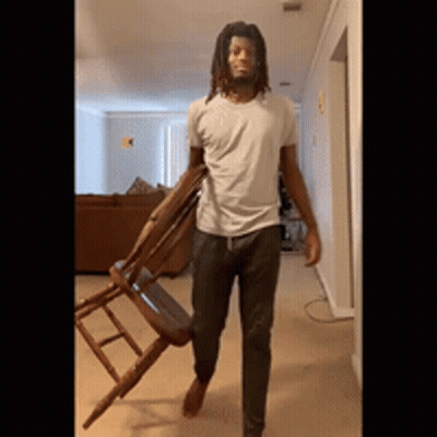 Man With Dreadlocks Carrying Wooden Chair GIF