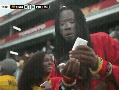 Man With Dreadlocks Holding Cell Phone At Soccer Game GIF