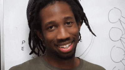 Man With Dreadlocks Smiling In Front Of PE Board GIF