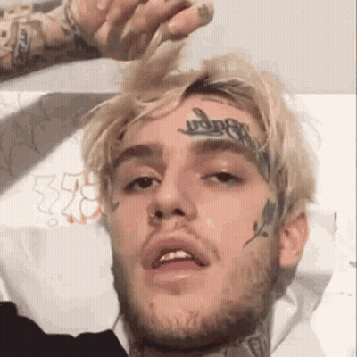Man With Face Tattoo Lying On Bed Looking At Camera GIF