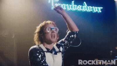 Man With Fist In Air In Front Of Rocketman Sign GIF