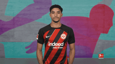 Man With Folded Hands In Front Of Bundesliga Mural GIF