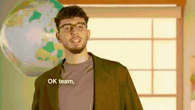 Man With Glasses And Beard Saying Ok Team In Front Of Globe GIF