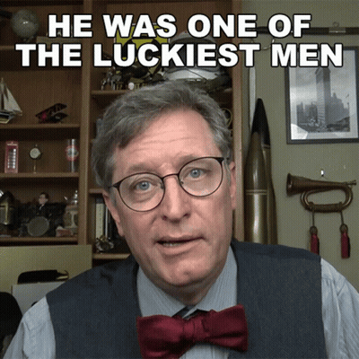 Man With Glasses and Bow Tie Says He Was One of the Luckiest Men in Front of Bookshelf