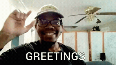 Man With Glasses And Hat Saying Greetings In Front Of Ceiling Fan GIF