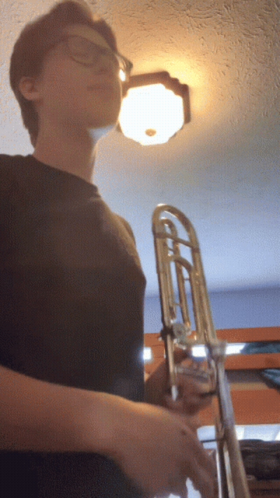 Man With Glasses Holding Trombone In Front Of Light GIF