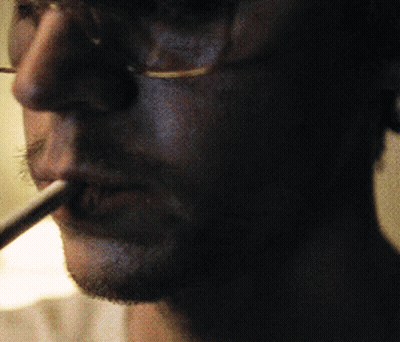 Man With Glasses Smoking Cigarette In Dark Room GIF