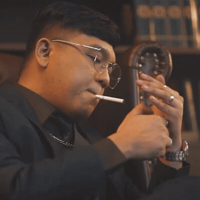 Man With Glasses Smoking Cigarette In Front Of Bookshelf GIF