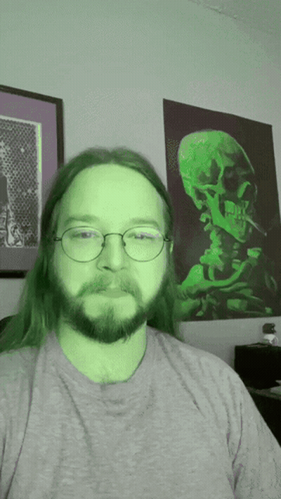 Man With Green Hair And Glasses In Front Of Skull Painting GIF